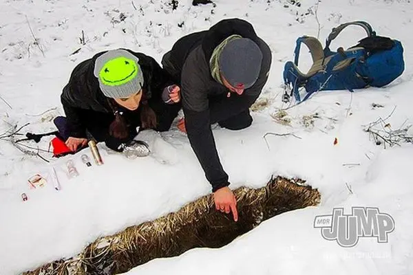 Zwei Personen knien im Schnee und betrachten eine Öffnung im Boden