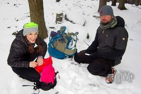 Zwei Personen sitzen im Schnee und packen Rucksäcke aus