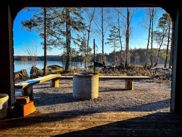 Blick auf Feuerstelle mit Sitzbänken und Wasser im Hintergrund