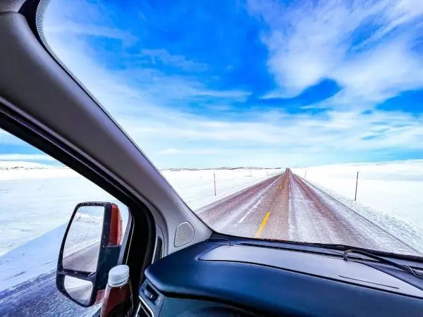 Blick aus einem Fahrzeug auf eine schneebedeckte Straße unter blauem Himmel