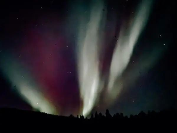 Farbenfrohe Lichtstrahlen erhellen den Nachthimmel über einer silhouettierten Landschaft