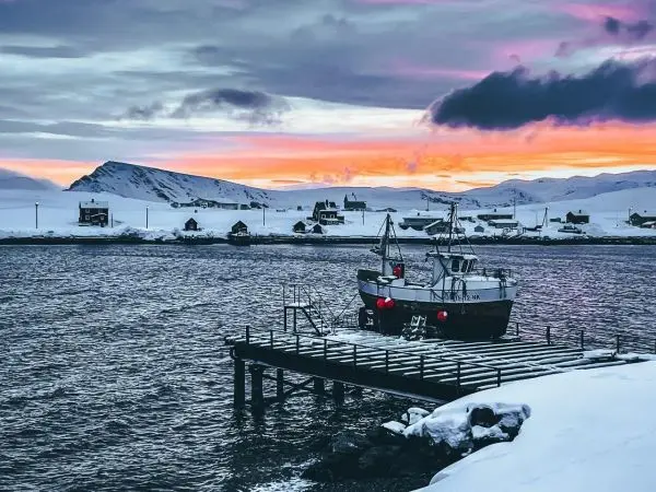 Fischerboot liegt an einem Steg im Schnee, Berge im Hintergrund