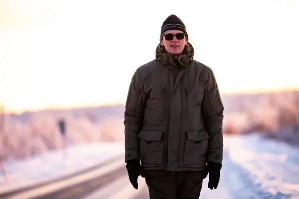 Mann in warmer Jacke und Mütze geht auf schneebedecktem Weg