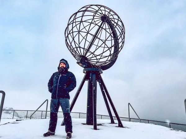 Mann steht im Schnee neben einer metallenen Globuskonstruktion
