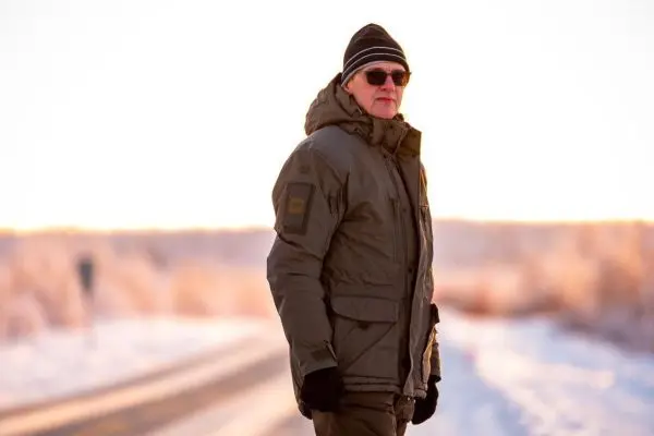 Person in warmer Jacke und Sonnenbrille auf einer Straße im Schnee