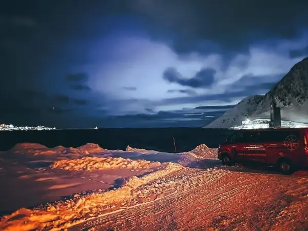 Schnee bedeckte Landschaft mit einem roten Fahrzeug und Bergen im Hintergrund