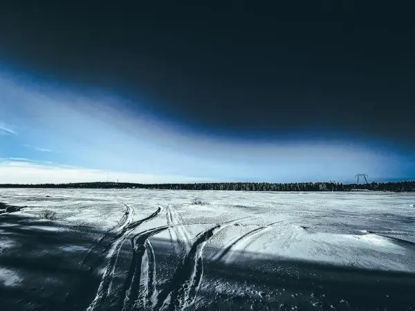 Schneebedeckte Fläche mit Spuren und bewaldetem Horizont im Hintergrund