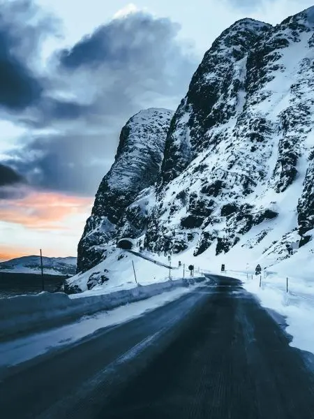 Schneebedeckte Straße zwischen hohen Felsen unter bewölktem Himmel