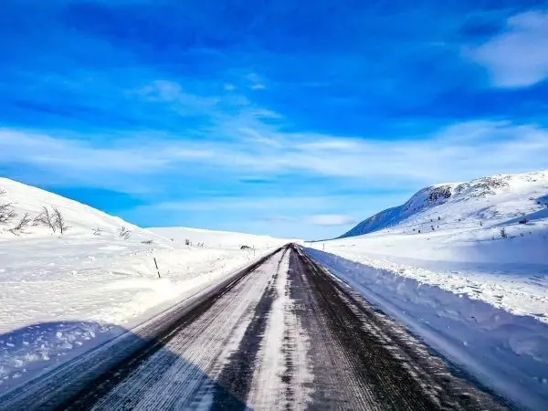 Schneebedeckte Straße zwischen Hügeln unter blauem Himmel