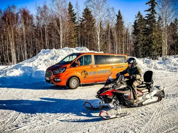 Schneemobil fährt auf verschneiter Fläche neben einem orangefarbenen Transporter