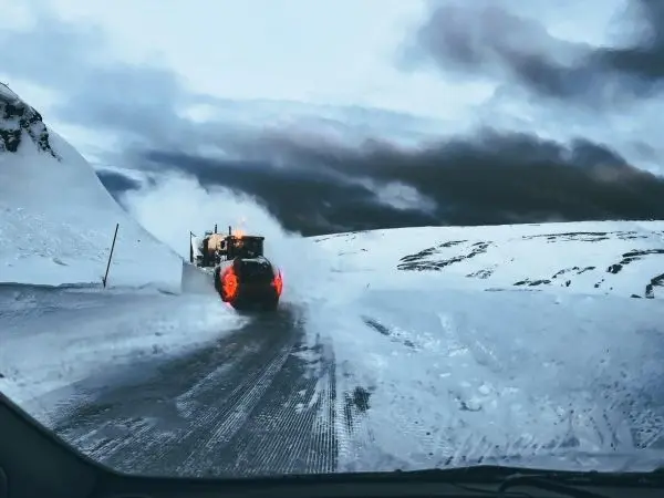 Schneepflug räumt verschneite Straße in bergiger Landschaft