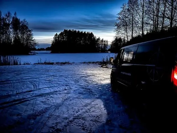 Schwarzer Van steht auf verschneitem Boden bei Dämmerung am Wasser