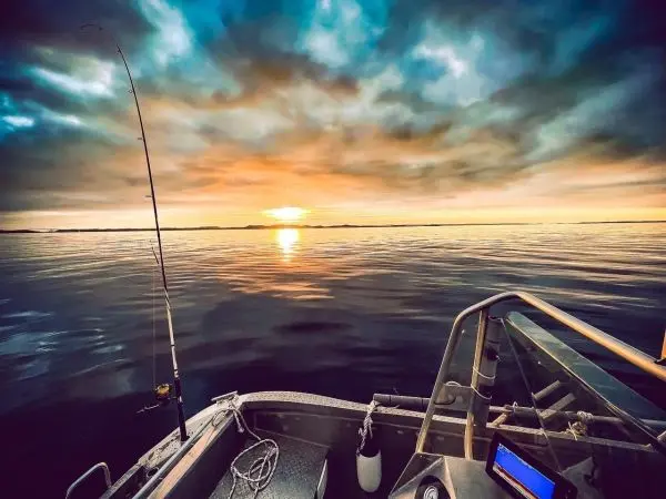 Anglerute steht in einem Boot, Sonnenuntergang spiegelt sich im Wasser
