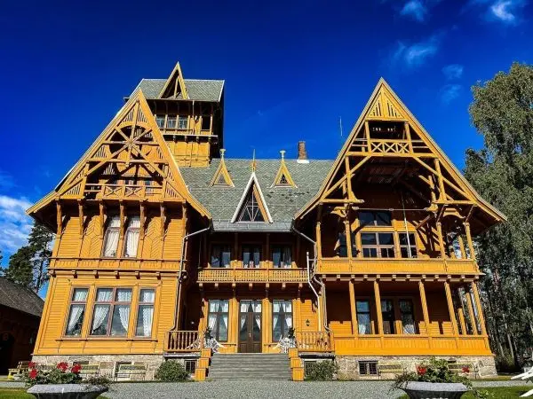 Holzhaus mit mehreren Erkern und spitzen Dächern vor blauem Himmel