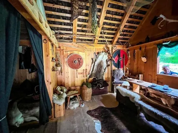 Innenansicht einer Holzhütte mit Schilden und Fellen