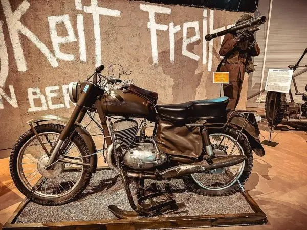 Motorrad in einem Museum, im Hintergrund eine Wand mit Schrift