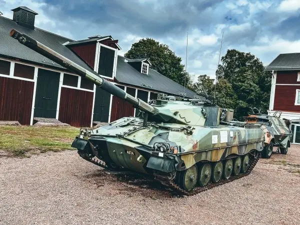 Panzer mit getarnter Lackierung steht auf einem Schotterplatz neben einem Gebäude