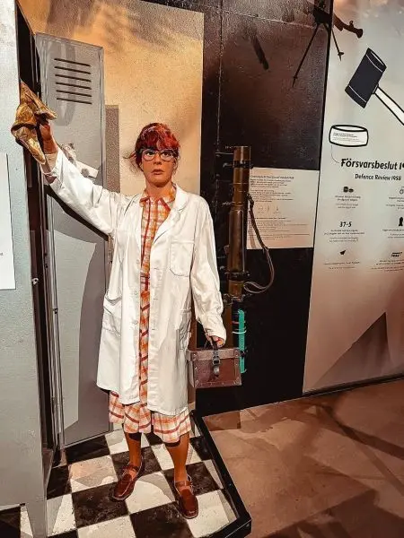 Puppe in Laborkleidung hält einen Koffer und eine Handschuh in einer Ausstellung