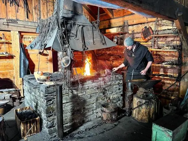 Schmied bearbeitet glühendes Metall am Amboss vor offener Feuerstelle
