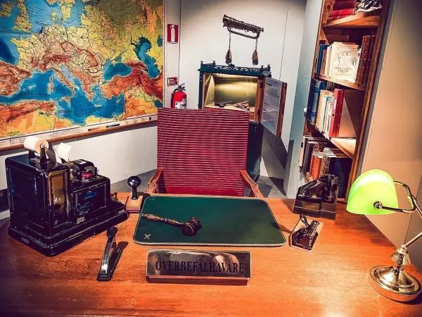 Schreibtisch mit Schreibmaschine, Stempel und grüner Lampe vor einer Weltkarte