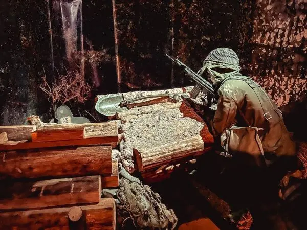 Soldat mit Gewehr lehnt sich an einen Holzstapel in einer Deckung