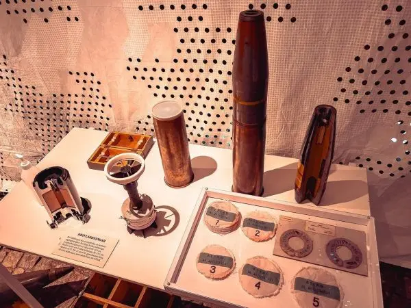 Verschiedene Artilleriegeschosse und deren Komponenten auf einem Tisch ausgestellt