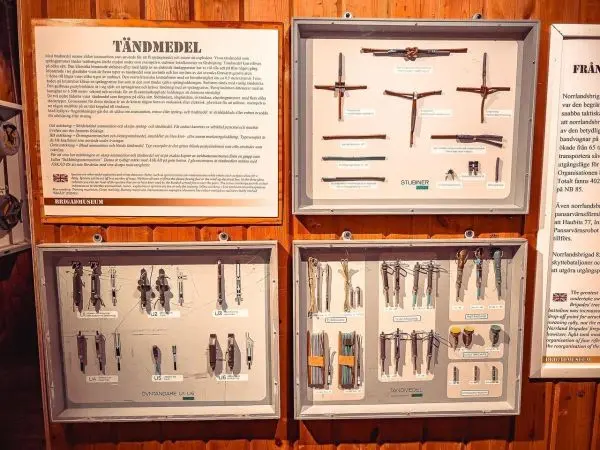 Verschiedene Zündmittel und Werkzeuge in Vitrinen an einer Wand aus Holz