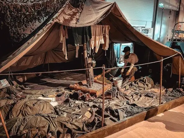 Zelt mit Ausrüstung und Kleidung, Person bearbeitet den Boden