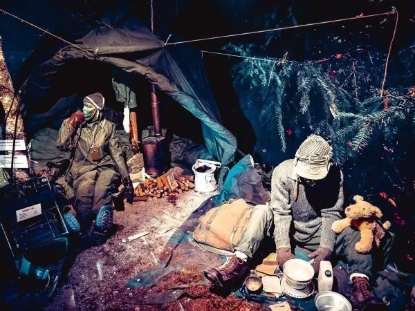 Zwei Personen sitzen in einer improvisierten Unterkunft mit Ausrüstung und Kochgeschirr