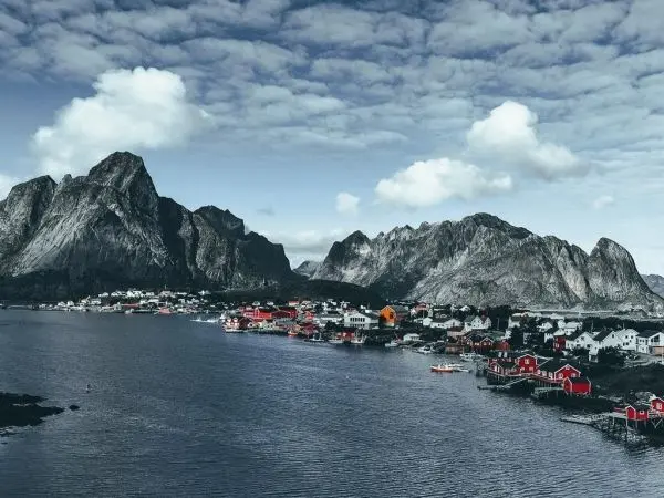 Bergige Küstenlandschaft mit bunten Häusern am Wasser und bewölktem Himmel