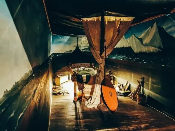 Ein Bett mit Vorhängen steht in einem Raum mit Wandmalereien von Bergen