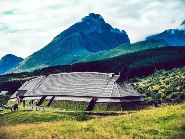 Holzbau mit schrägem Dach vor Berglandschaft und bewaldetem Hang
