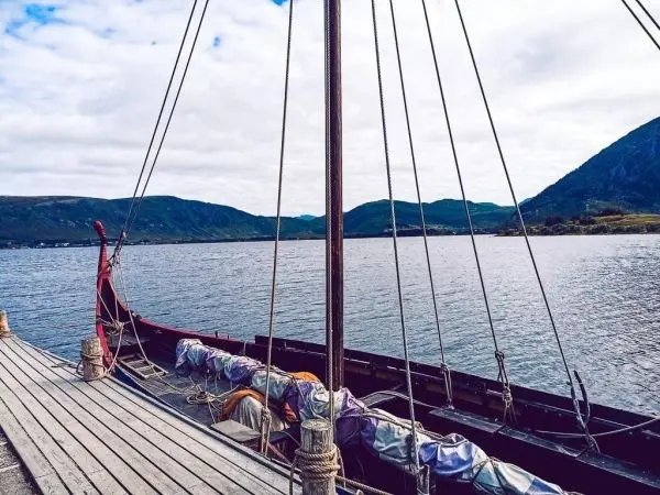 Holzboot mit Segel liegt am Steg, Blick auf ruhiges Wasser und Berge