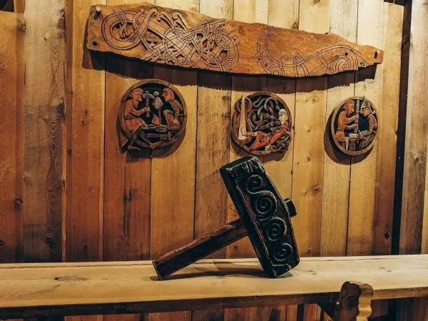 Holzhammer liegt auf einem Tisch vor einer Holzwand mit Schnitzereien