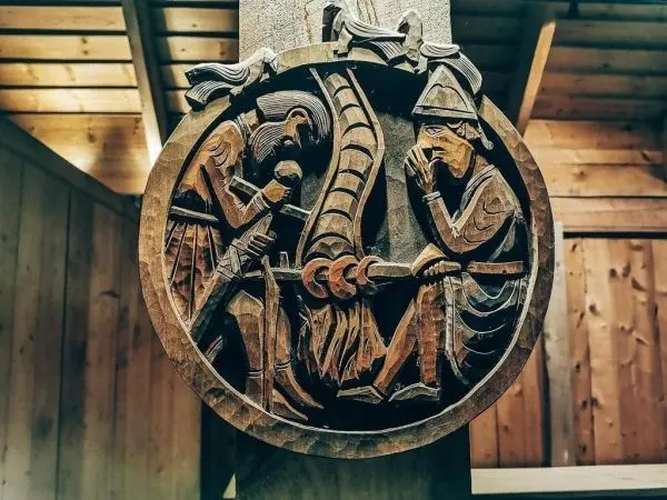 Holzrelief zeigt zwei Figuren, die an einem gemeinsamen Objekt arbeiten