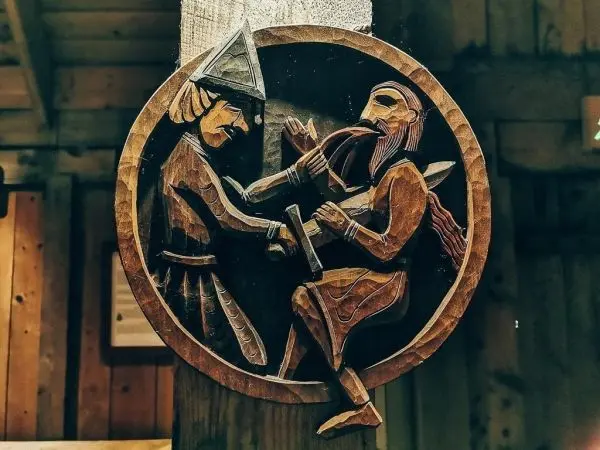 Holzrelief zeigt zwei kämpfende Figuren mit Schwertern in einer runden Umrandung
