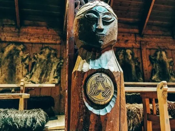 Holzskulptur mit geschnitztem Gesicht und keltischem Symbol im Hintergrund