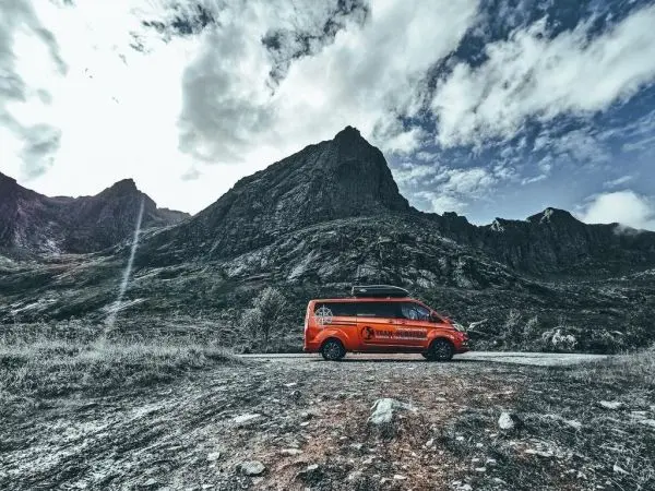 Oranger Van steht auf einer Straße vor einer bergigen Landschaft mit Wolken