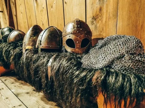 Reihe von Rüstungen und Helmen auf einem Fell über einer Holzbank