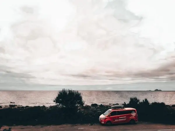 Roter Van parkt am Ufer mit Blick auf das Meer und bewölkten Himmel