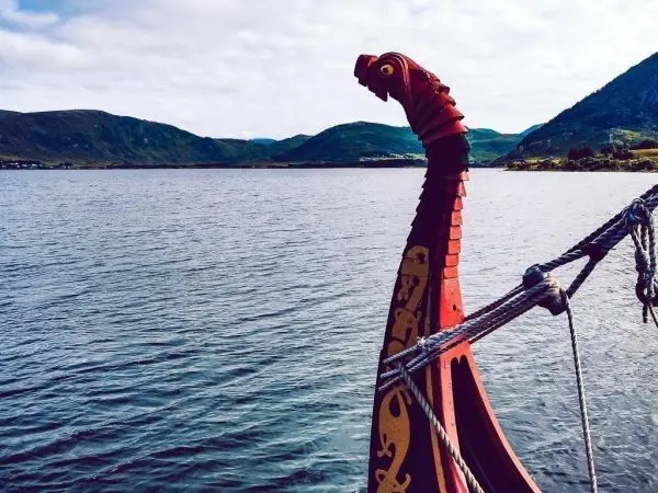 Schiff mit Drachenkopf auf Wasseroberfläche vor hügeliger Landschaft
