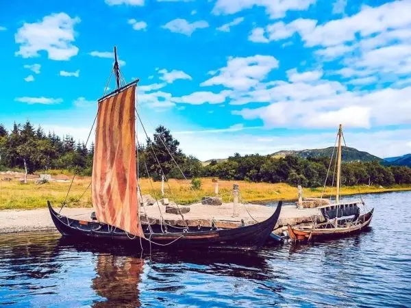 Zwei Boote mit Segeln liegen am Ufer eines Gewässers