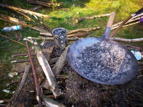 Asche in einer großen Pfanne auf einem Untergrund aus Ästen und Holzstücken