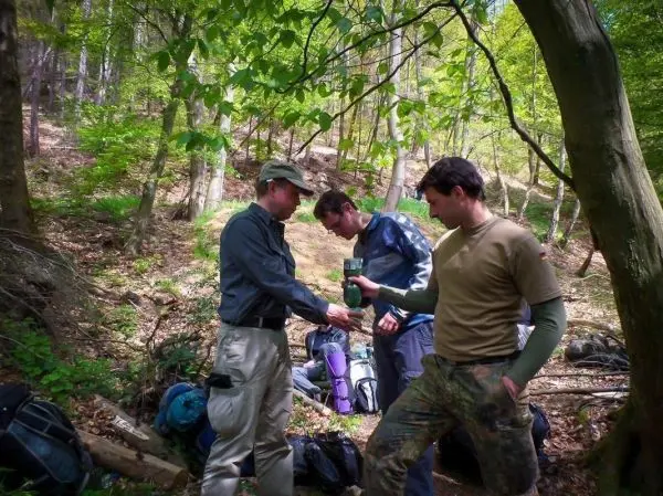 Drei Personen stehen im Wald und tauschen Ausrüstung aus
