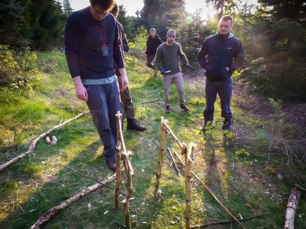 Gruppe betrachtet selbstgebaute Schlagfalle aus Ästen im Wald