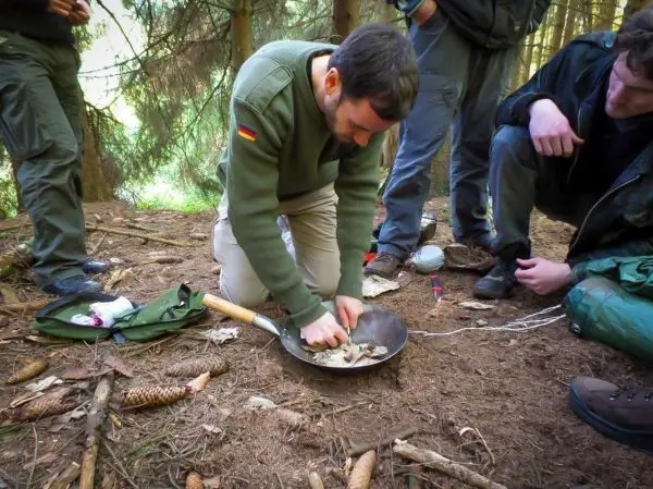 Mann bereitet Nahrung in einer Pfanne auf dem Boden vor, umgeben von anderen Personen
