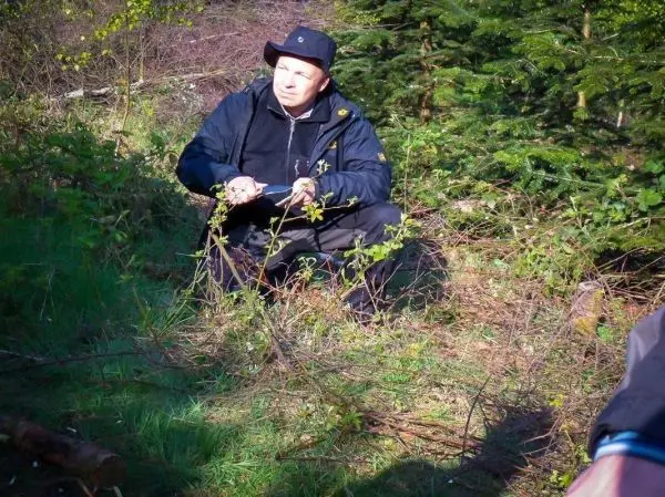Mann sitzt im Gras und hält ein Messer in der Hand