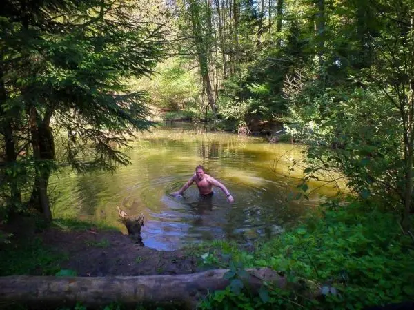 Mann steht im Wasser eines kleinen Teiches, umgeben von Bäumen und Pflanzen