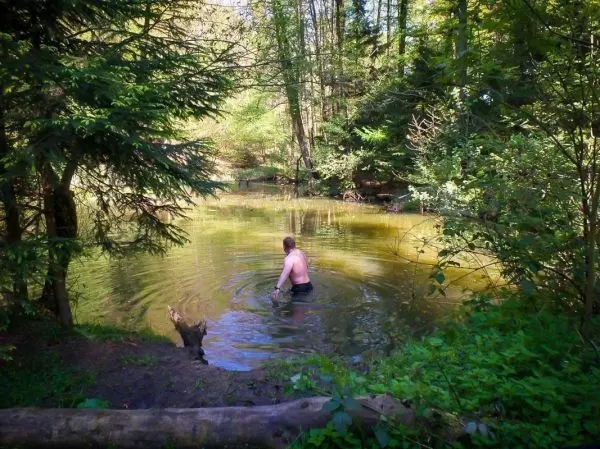 Mann steht im Wasser eines kleinen Teichs, umgeben von Bäumen und Pflanzen