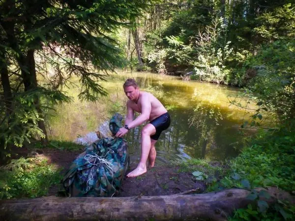 Mann zieht eine camouflagefarbene Tasche am Ufer eines Gewässers
